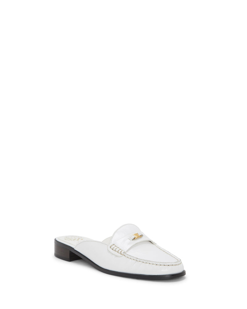 The Vince Camuto Cobby Mule is a white leather slip-on loafer featuring a moc toe, low dark block heel, beige stitching, and a small gold accent on the top, displayed against a plain white background.
