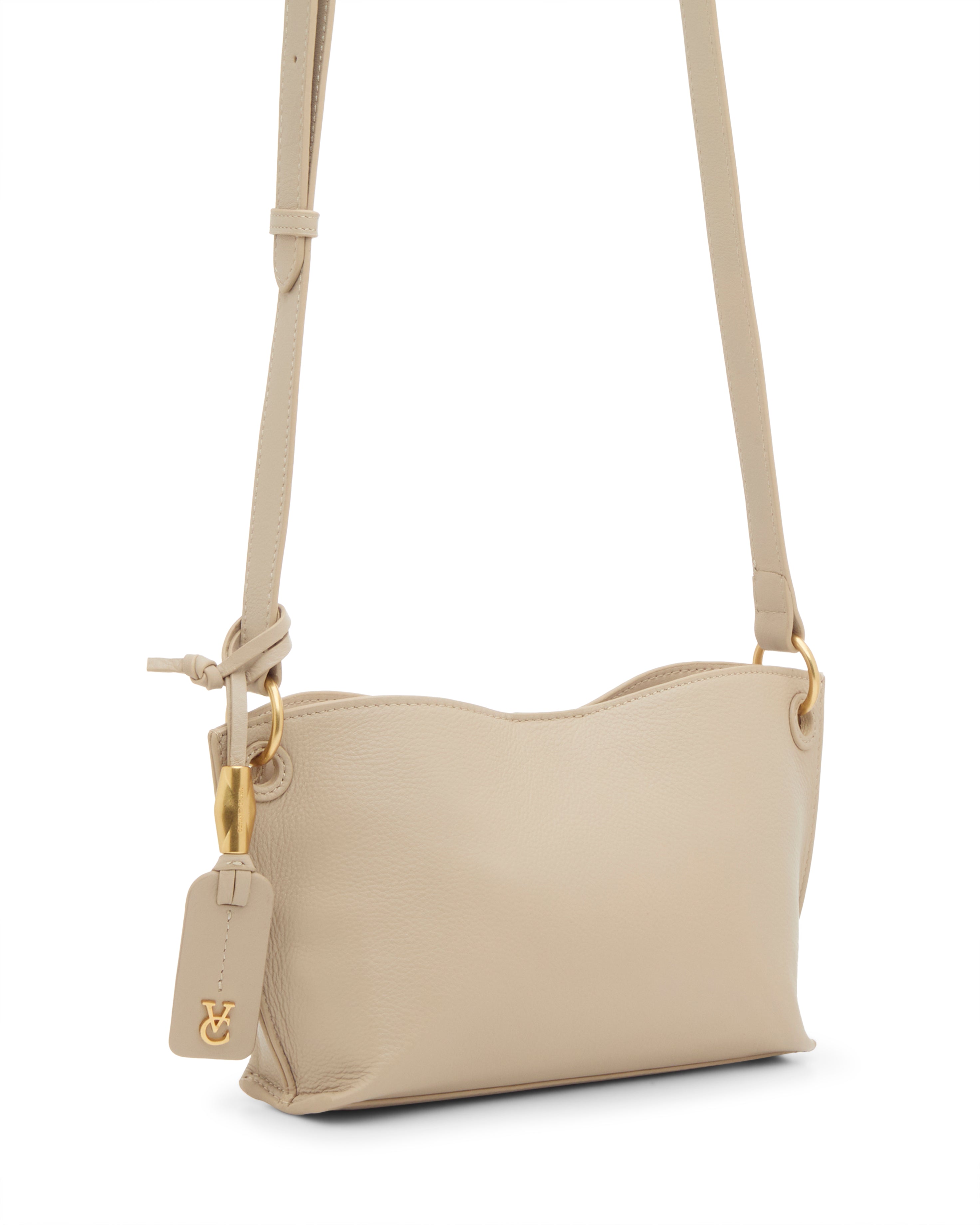 The Vince Camuto Ellah Crossbody Bag is a small beige leather bag with gold hardware, a gold logo charm, and an adjustable strap, shown against a white background.