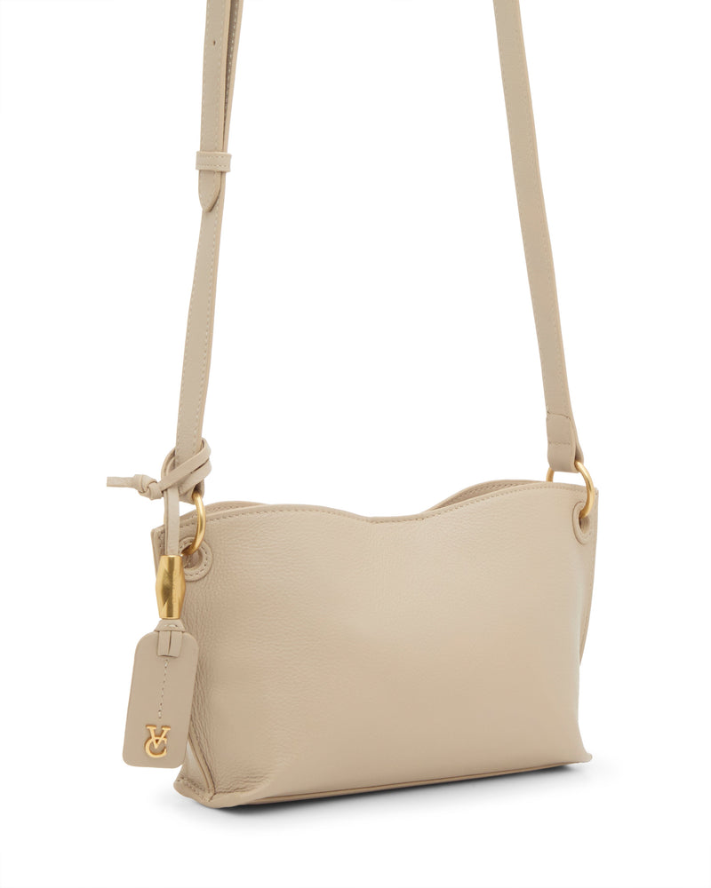 The Vince Camuto Ellah Crossbody Bag is a small beige leather bag with gold hardware, a gold logo charm, and an adjustable strap, shown against a white background.