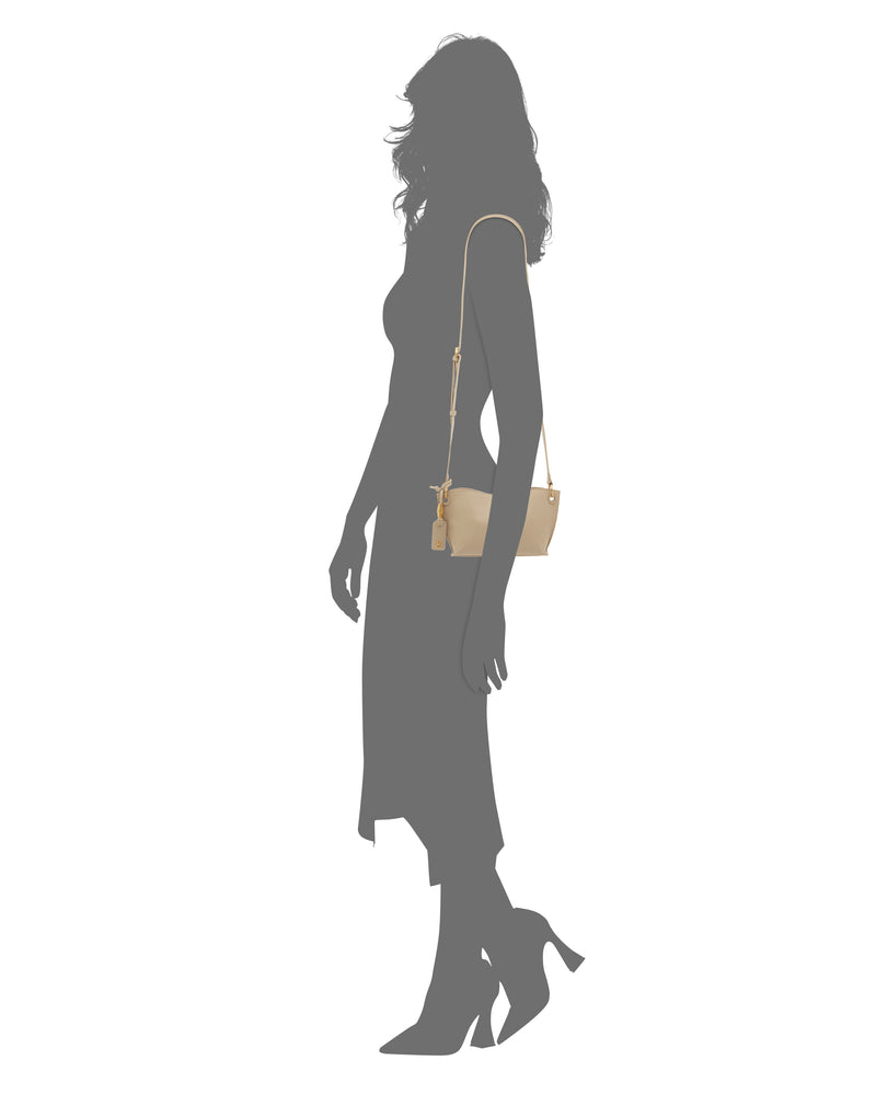 A silhouette of a woman in a mid-length dress and heels holds the Vince Camuto Ellah Crossbody Bag—a small beige shoulder bag with a long strap, shown as the only item in color.