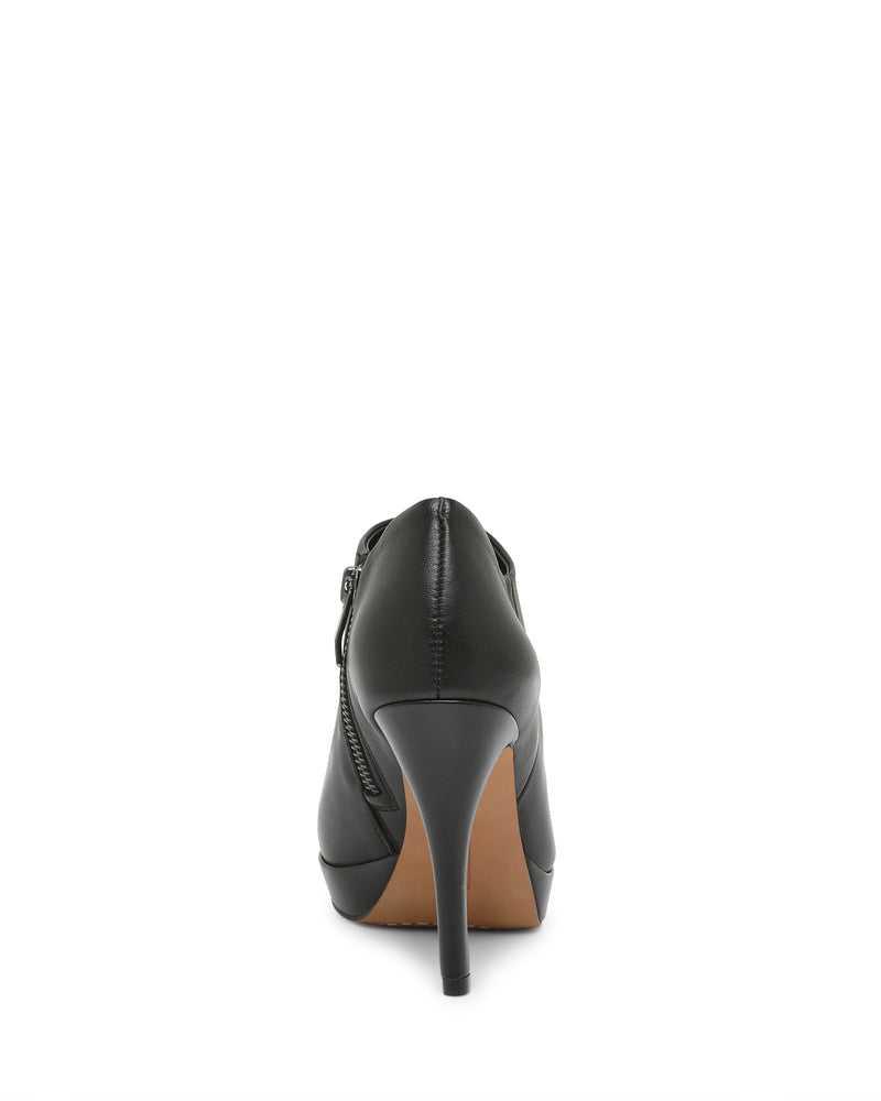 A rear view of the Vince Camuto Elvin Bootie in black, showcasing its side zipper detail, brown outsole, and sky-high heel, photographed against a white background.