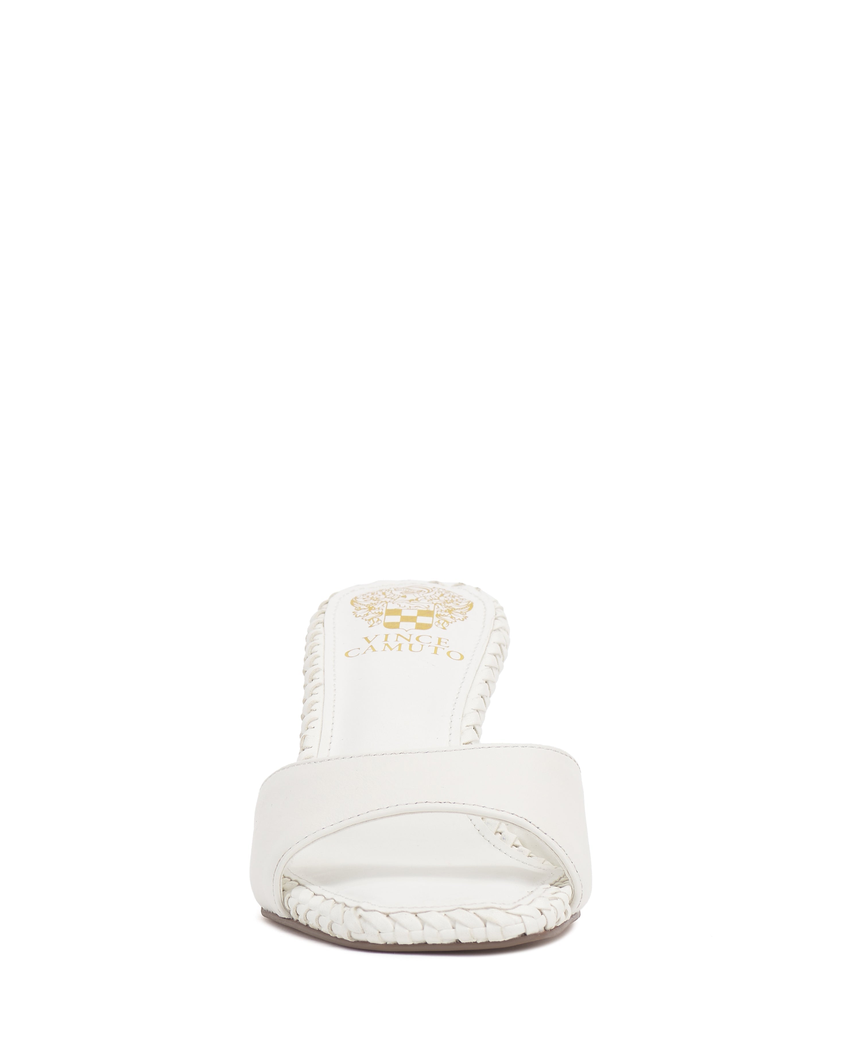 Front view of the Emmla Mule by Vince Camuto—a white open-toe sandal with a single strap and braided edges. A gold logo decorates the insole, highlighting this modern, elegant footwear against a plain white background.