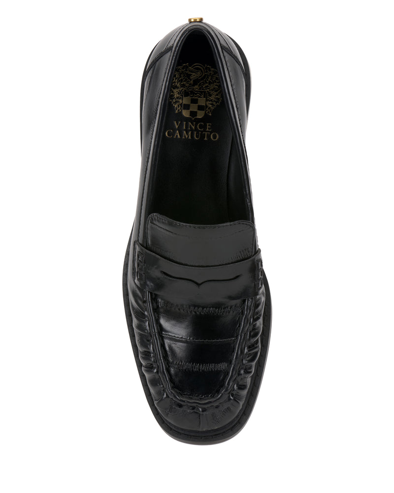A top view of the black leather Vince Camuto Eshnie Block Heel Loafer shows a penny strap, visible stitching, and subtle reptile embossing. The insole features a gold Vince Camuto logo and crest on this textured classic design.
