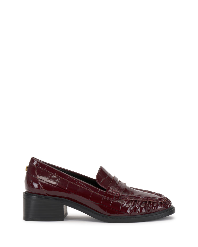 The Eshnie Block Heel Loafer by Vince Camuto features burgundy crocodile-embossed leather, a low block heel, and a black sole, shown in side profile on a white background.