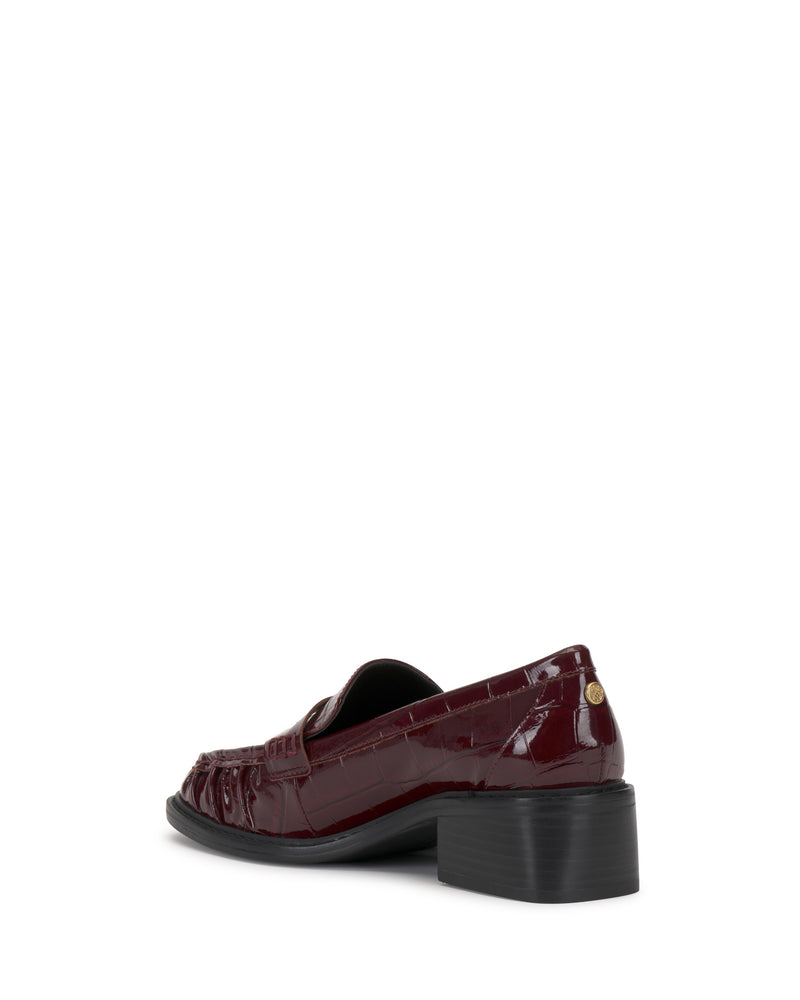 The Vince Camuto Eshnie Block Heel Loafer in maroon crocodile texture is shown from the back, highlighting its low block heel and small round metallic detail near the heel counter.