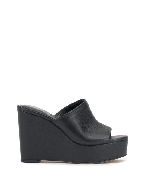 The Etta Wedge Sandal by Vince Camuto features black textured leather, a minimal single band, an open toe, and a thick platform. Y2K-inspired with a bold yet understated design, it offers modern style without visible embellishments.