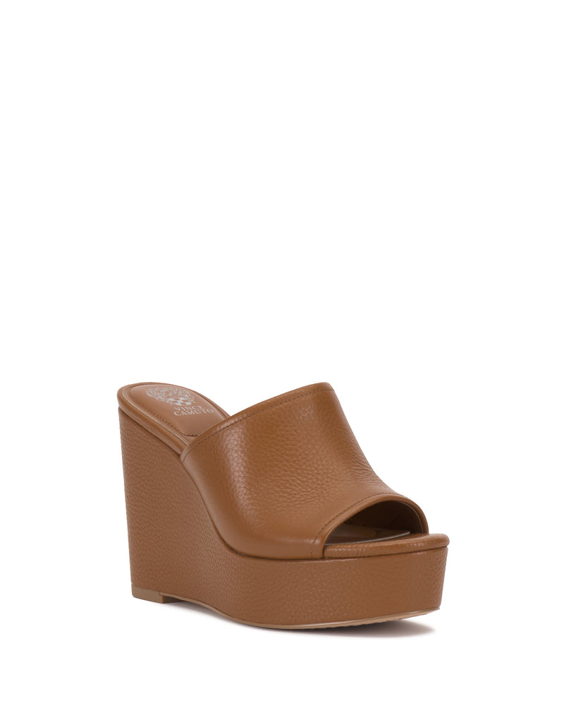The Etta Wedge Sandal by Vince Camuto is a brown, single-banded open-toe slip-on with a high leather wedge heel and textured finish, photographed against a white background.
