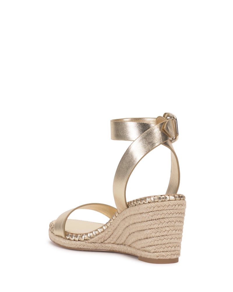 The Fainel Espadrille Wedge Sandal by Vince Camuto features a gold metallic finish, open toe, minimalist design, bold buckle ankle strap, and braided jute wrapping—perfect for effortless summer style.