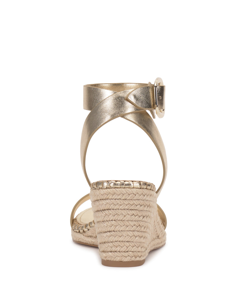 The Vince Camuto Fainel Espadrille Wedge Sandal features metallic gold ankle straps with a bold buckle, a woven textured platform, open heel design, and signature espadrille wedge heel—perfect for summer style.