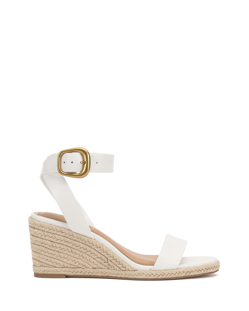 The Felia Espadrille Wedge Sandal by Vince Camuto features a white leather upper, braided jute espadrille heel, ankle strap with a large gold buckle, open toe, and a medium heel for an elegant, versatile look.