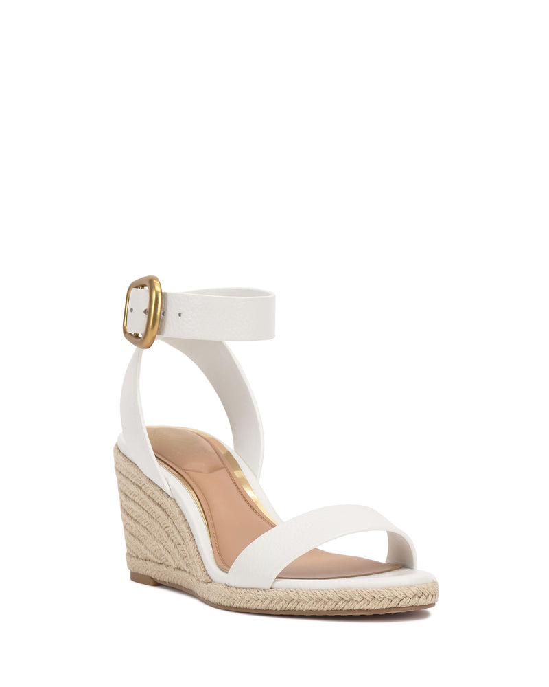 The Felia Espadrille Wedge Sandal by Vince Camuto features a white leather upper, ankle strap with gold buckle, espadrille wedge heel, single toe strap, neutral insole, and an open-toe design for effortless style.