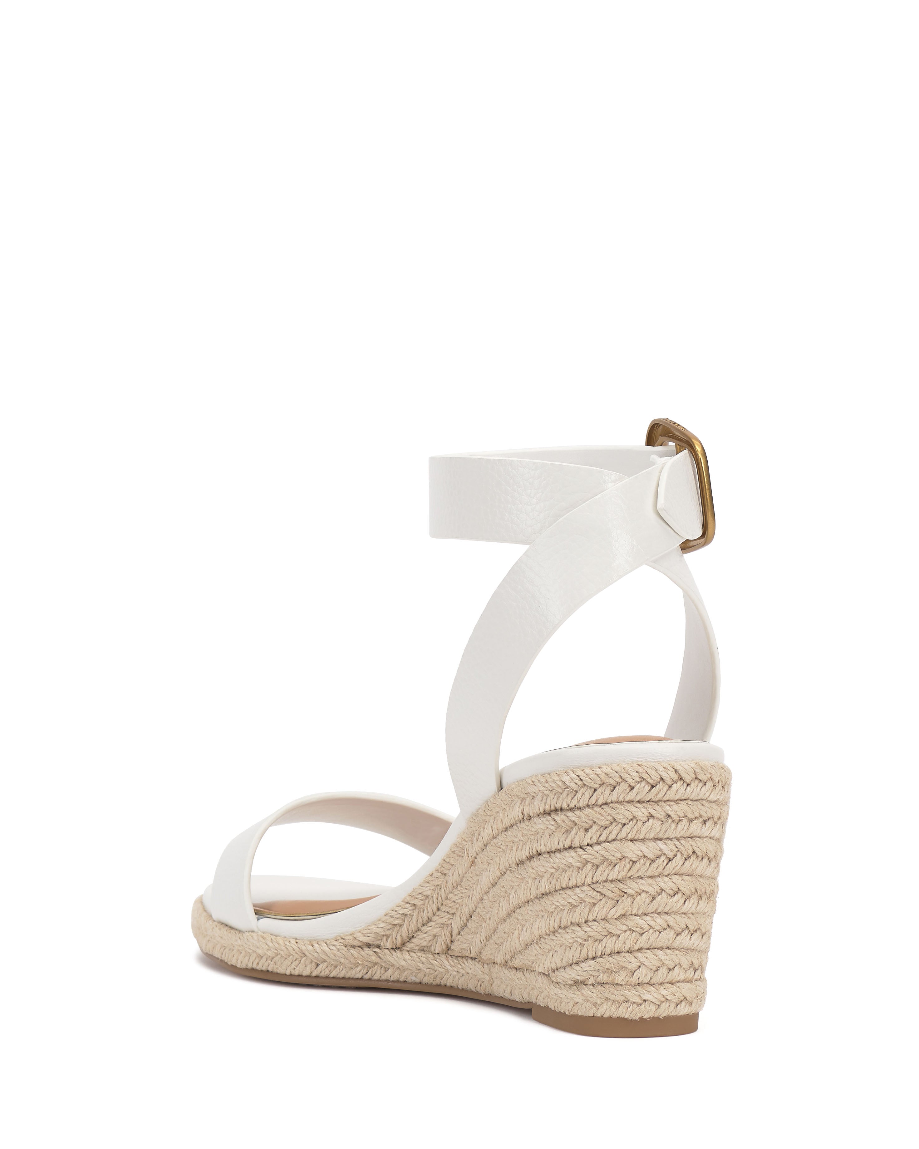 The Vince Camuto Felia Espadrille Wedge Sandal features a white leather upper with strappy ankle buckle, a woven espadrille-style sole, and a low wedge heel, shown from the rear side view.