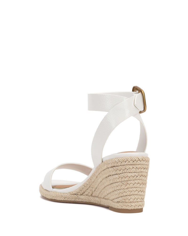 The Vince Camuto Felia Espadrille Wedge Sandal features a white leather upper with strappy ankle buckle, a woven espadrille-style sole, and a low wedge heel, shown from the rear side view.