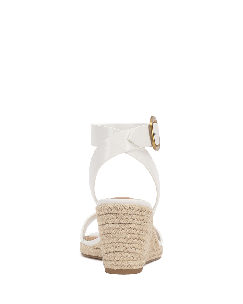 Back view of the Vince Camuto Felia Espadrille Wedge Sandal, featuring a white leather upper, crisscross ankle straps with gold buckle, and espadrille heel, shown against a plain white background.