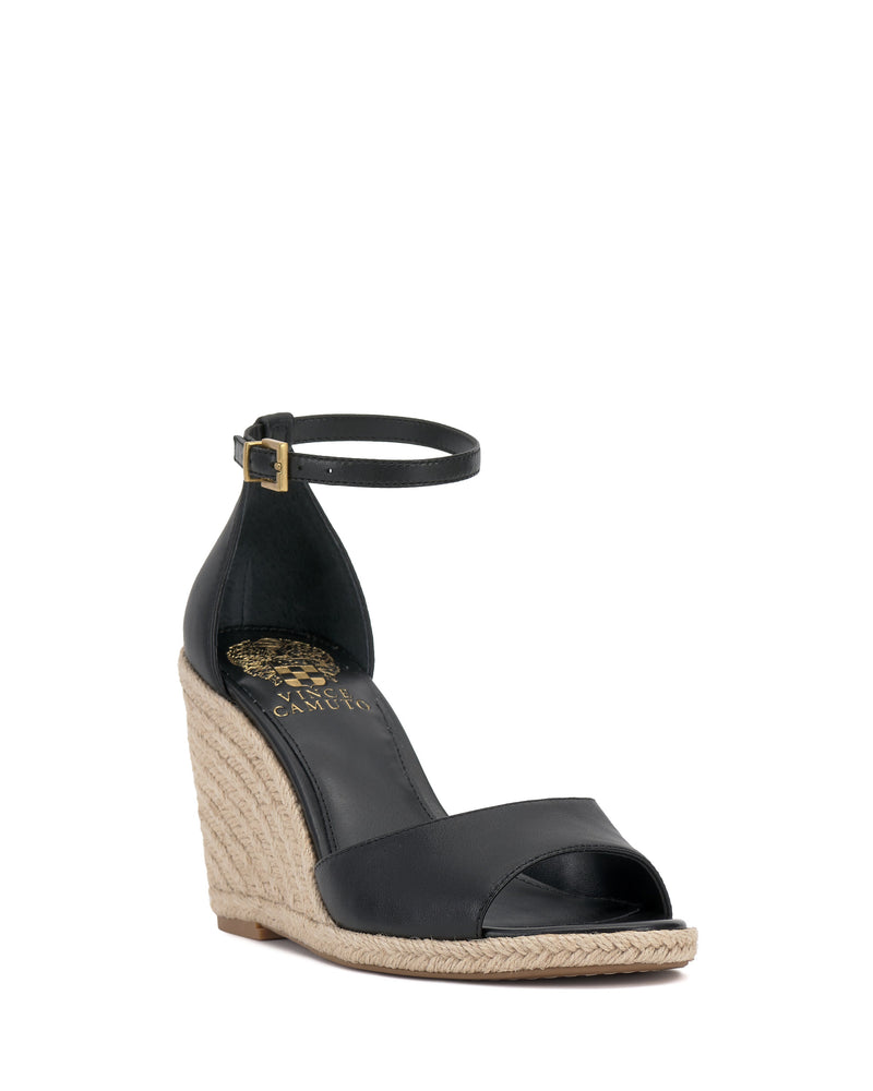 The Vince Camuto Felyn Espadrille Wedge Sandal is a black open-toe design with an ankle strap and buckle, featuring a woven jute wedge heel, gold branded insole, and an elegant summery style.
