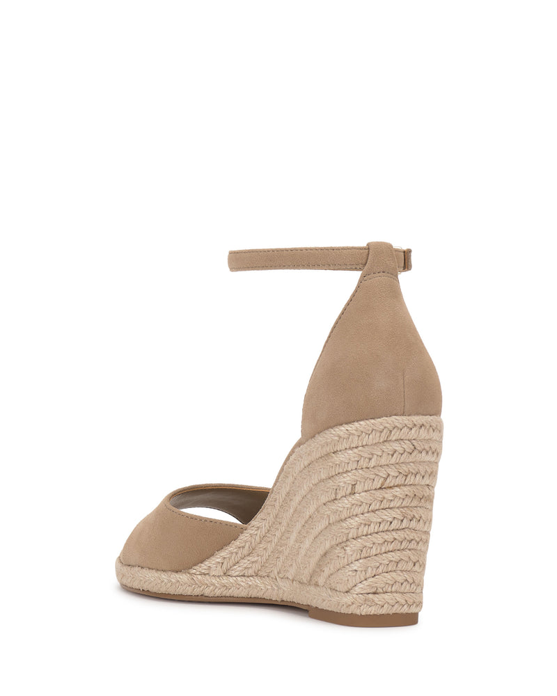 The Vince Camuto Felyn Espadrille Wedge Sandal features a tan, closed-toe design with an ankle strap, braided jute platform heel, and suede-like upper. The back view showcases the woven espadrille texture.