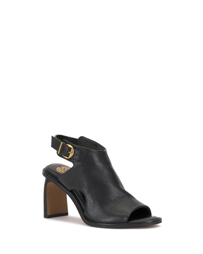 The Fezisha Sandal by Vince Camuto is a black leather open-toe shoe with cutout sides, a mid-height block heel, and an adjustable ankle strap featuring a gold buckle. A small gold emblem decorates the insole near the heel.