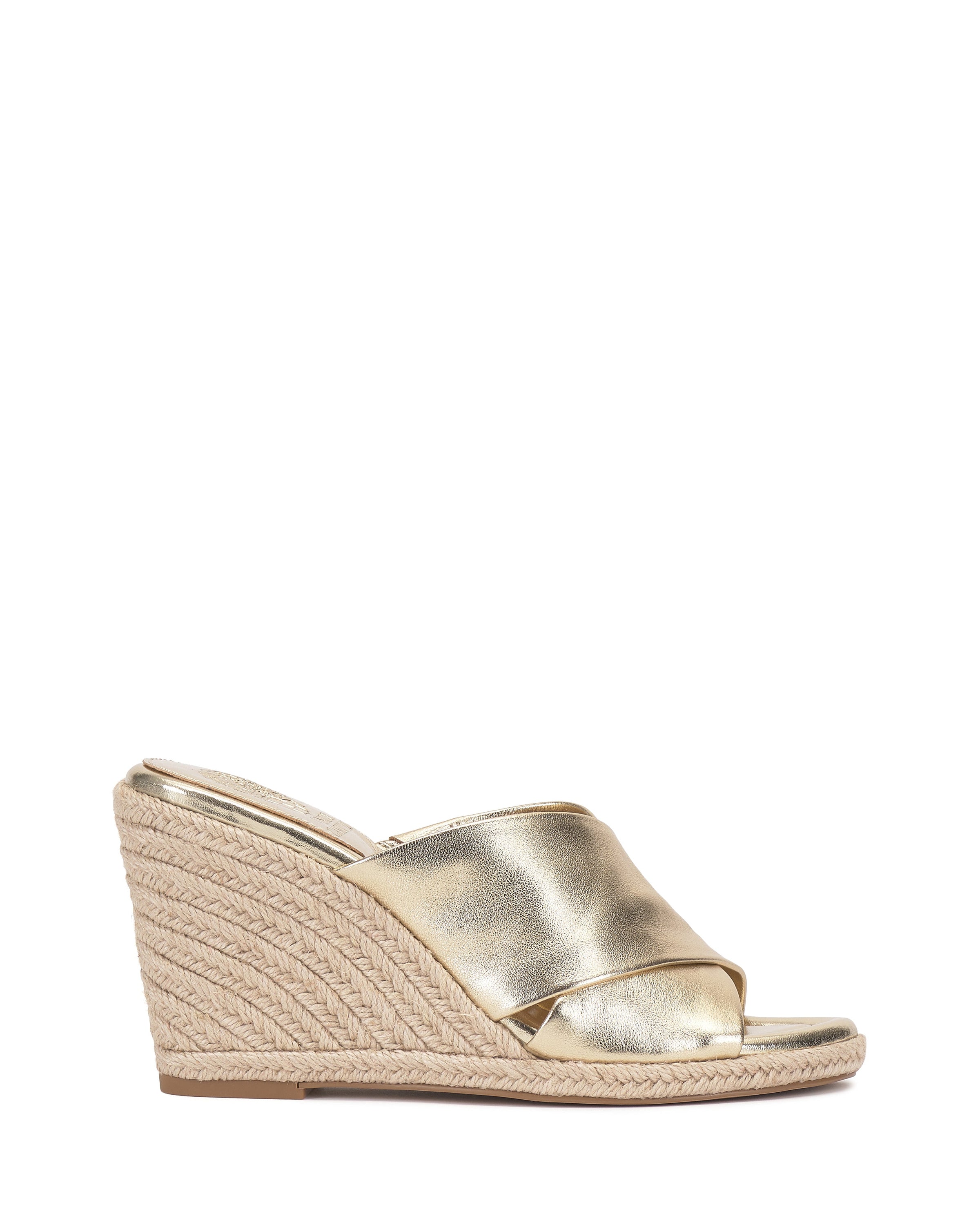 The Fisella Espadrille Wedge Sandal by Vince Camuto is a gold slip-on with crisscross leather straps and a braided espadrille platform wedge, shown on a white background.