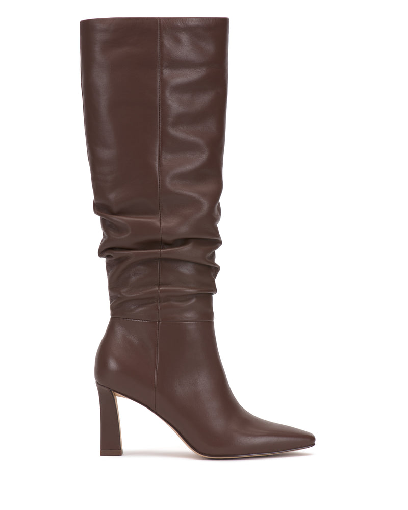 The Genisa Narrow Calf Slouchy Knee High Boot by Vince Camuto, featuring a tall silhouette in brown leather with a pointed toe and high block heel, is photographed from the side against a white background.