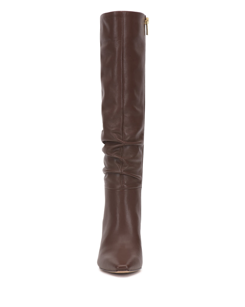 The Genisa Narrow Calf Slouchy Knee High Boot by Vince Camuto is a brown leather boot featuring a slightly slouched shaft and a gold zipper at the top, displayed from the front against a white background.
