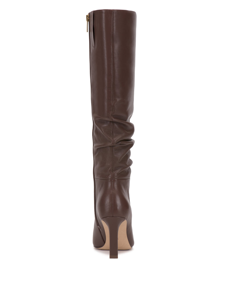 The Vince Camuto Genisa Narrow Calf Slouchy Knee High Boot is a tall, brown leather boot with a slouchy shaft, pointed toe, and high heel, shown from the back against a white background.