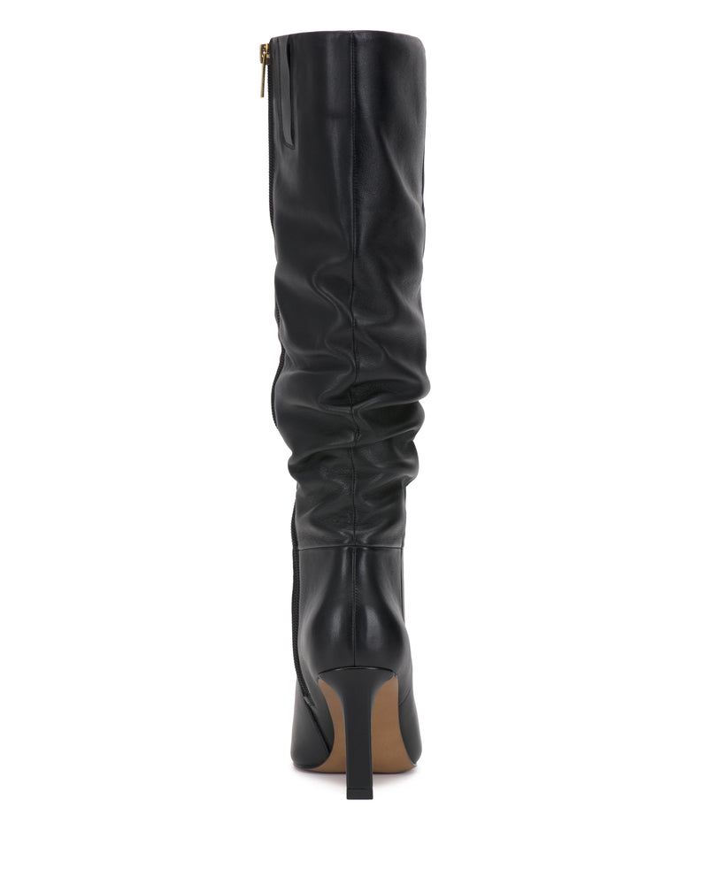The Vince Camuto Genisa Slouchy Knee High Boot, crafted in black leather with a slouchy shaft, pointed toe, stiletto heel, and side zipper, is displayed from a direct rear view against a white background.