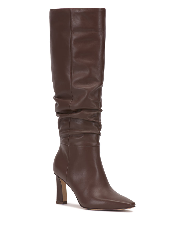 The Genisa Slouchy Knee High Boot by Vince Camuto is a tall brown leather boot featuring a pointed toe, slouchy shaft, and high block heel. With its sleek, modern design and minimal detailing, this boot is perfect for fashion-forward looks.