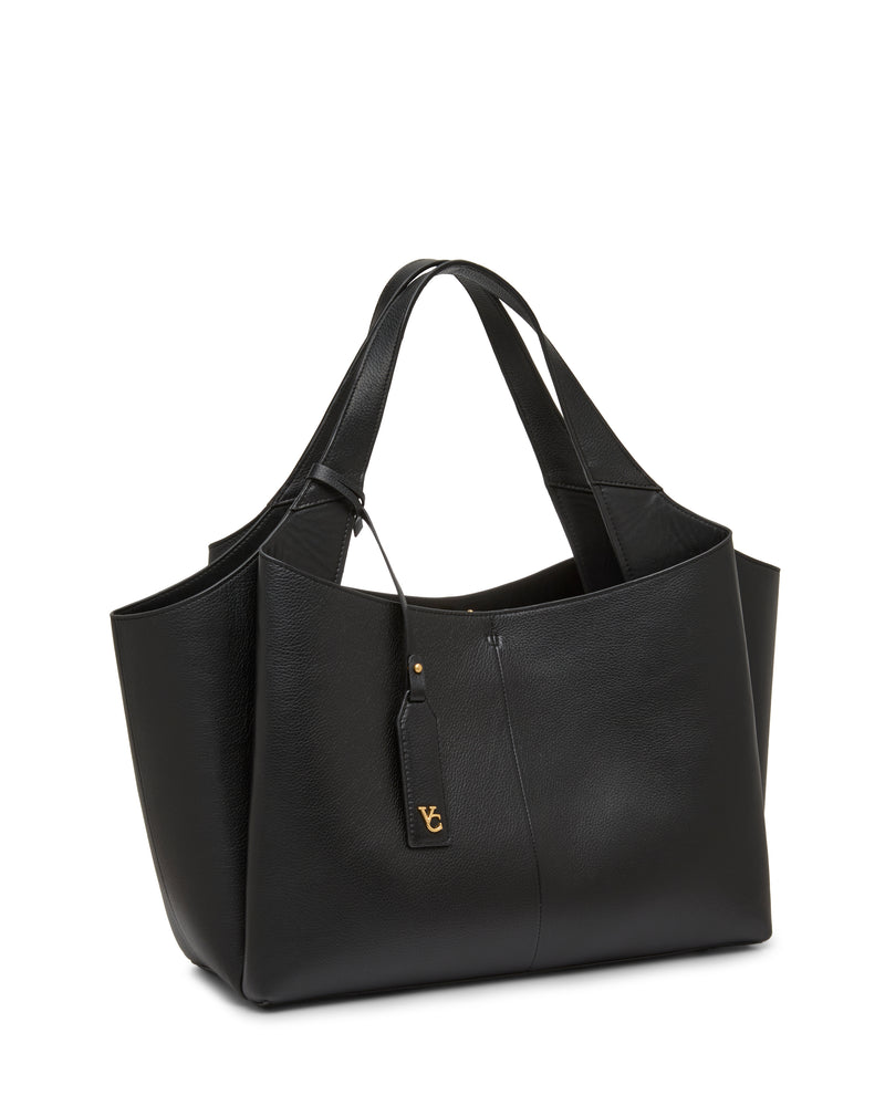 The Gilda Tote Bag by Vince Camuto is a spacious black leather tote featuring double handles, side pockets, and a gold-tone logo tag attached by a small strap. It offers a structured yet slightly slouchy silhouette.