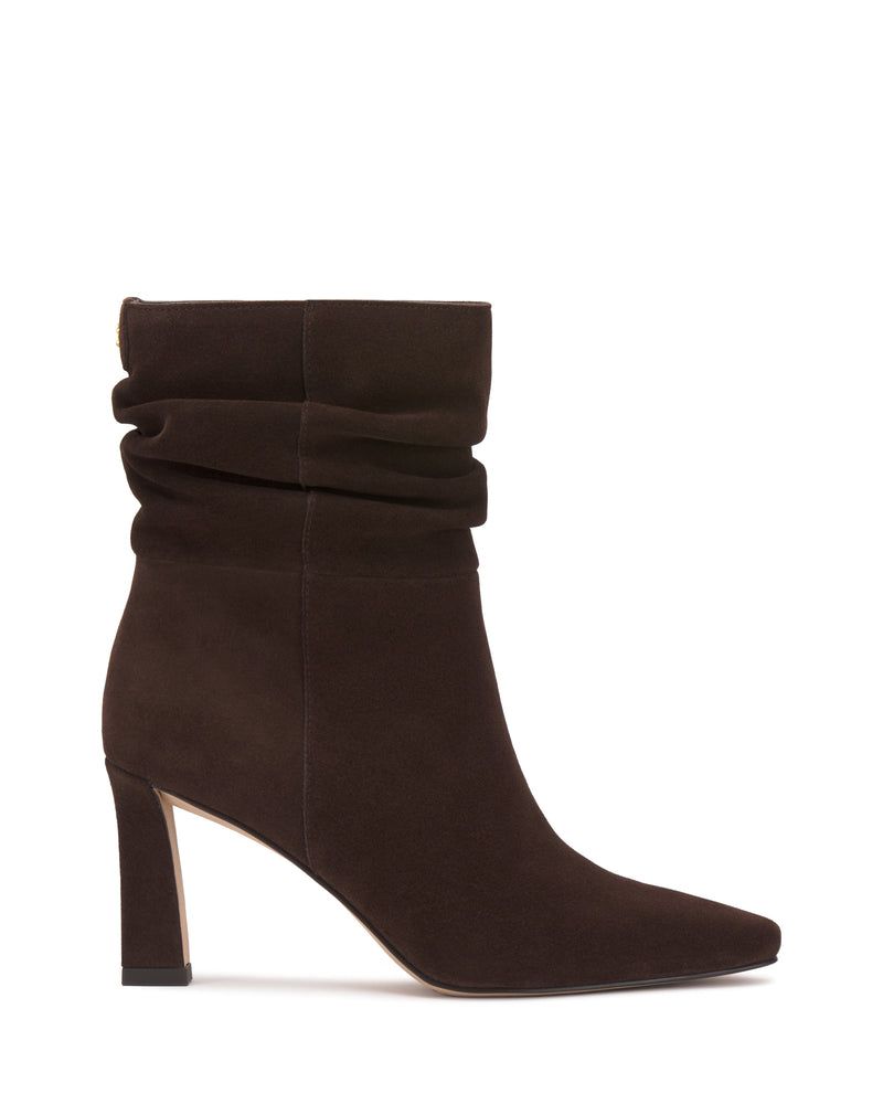 The Vince Camuto Grenna Slouchy Bootie is a brown suede ankle boot featuring a slouchy shaft, pointed toe, and high block heel, displayed on a white background.