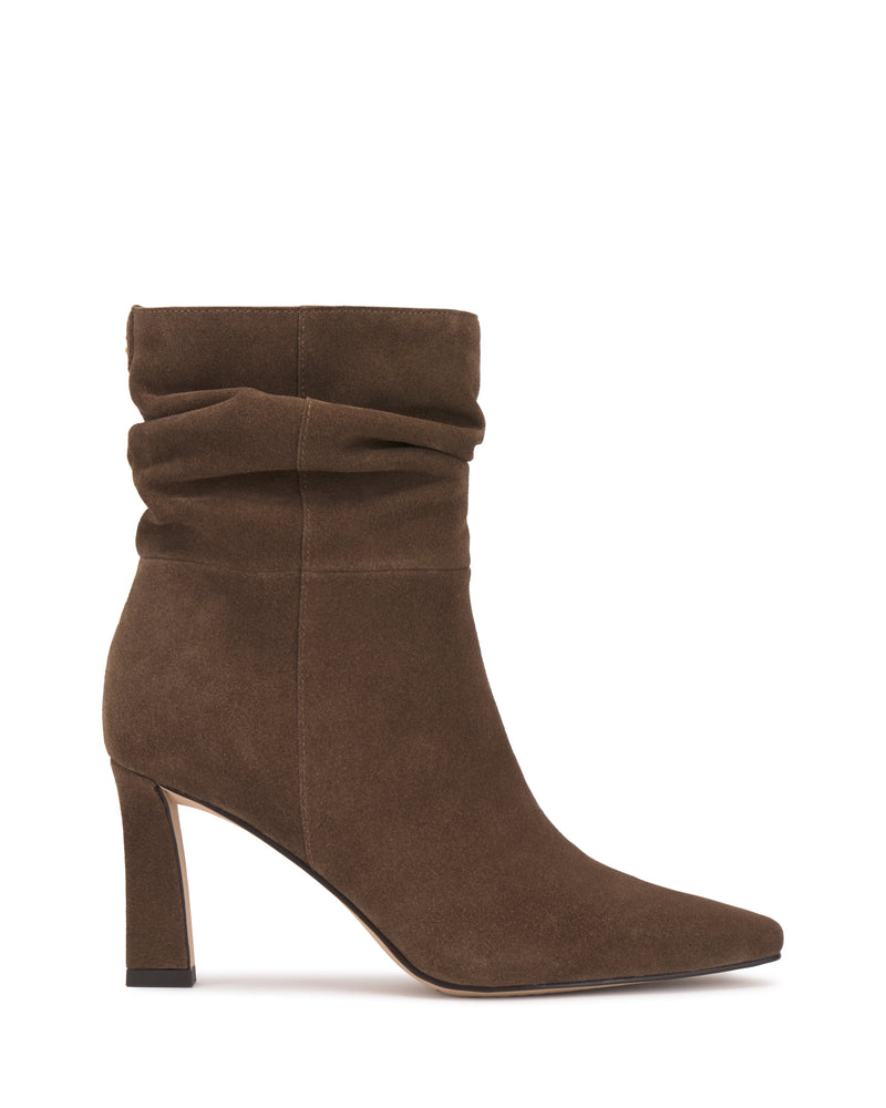 The Vince Camuto Grenna Slouchy Bootie is a brown suede ankle boot featuring a slouchy shaft, pointed toe, and high block heel, displayed in a side profile against a white background.