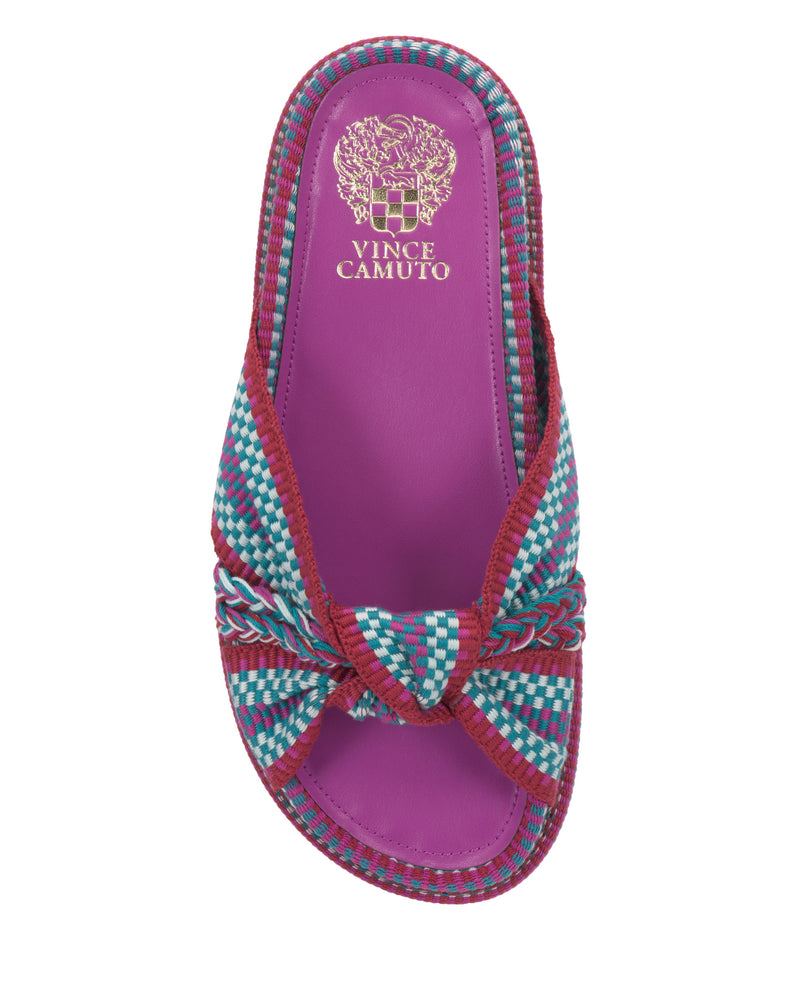 The Vince Camuto Gryfynn Slide features a magenta footbed, woven multi-colored straps in teal, white, and red with a knotted front design, cushioned sole for comfort, and gold logo detail on the heel for a summery style.