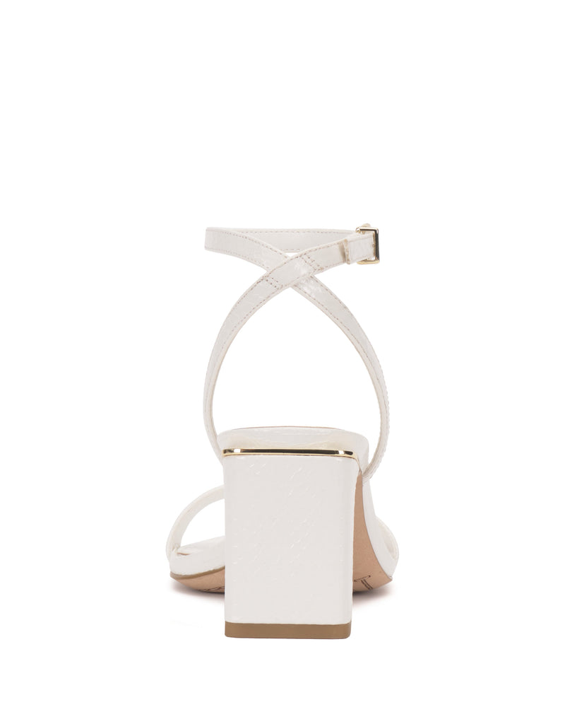 The Vince Camuto Hamda Sandal is a minimalist block-heel shoe seen from the back, showcasing crisscross adjustable ankle straps with a buckle and metallic gold accents on the heel edge and sole.
