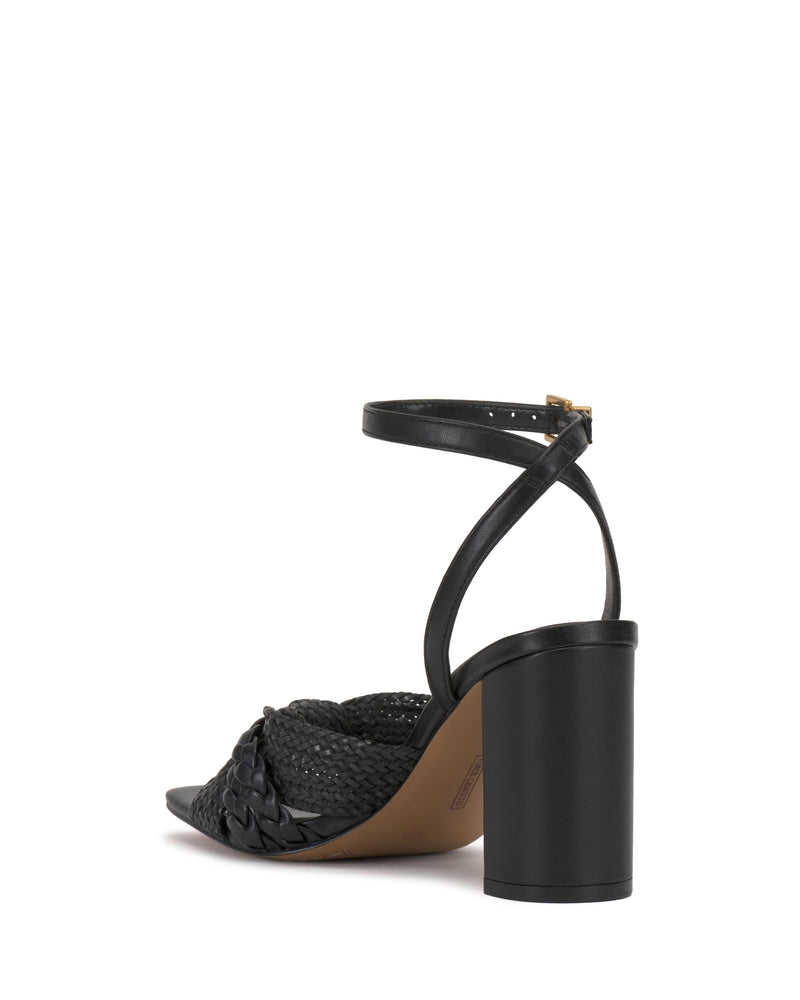 The Vince Camuto Hanlea Sandal features a black block heel, woven braided toe strap, and adjustable buckle ankle strap, shown on a white background.