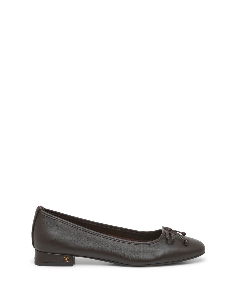 The Jenlea Ballet Flat by Vince Camuto is a dark brown leather shoe with a low block heel, highlighted by a charming bow accent on the toe and a gold detail on the heel. It is shown from the side against a white background.