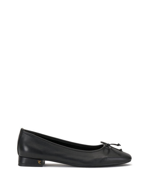 The Vince Camuto Jenlea Ballet Flat features black leather, a low heel, rounded toe, front bow, and subtle gold logo on the outer heel. Displayed against a white background.