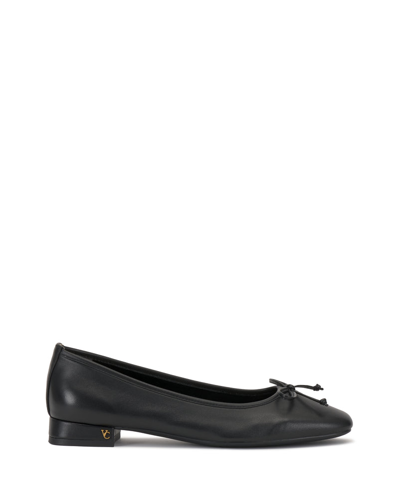 The Vince Camuto Jenlea Ballet Flat features black leather, a low heel, rounded toe, front bow, and subtle gold logo on the outer heel. Displayed against a white background.