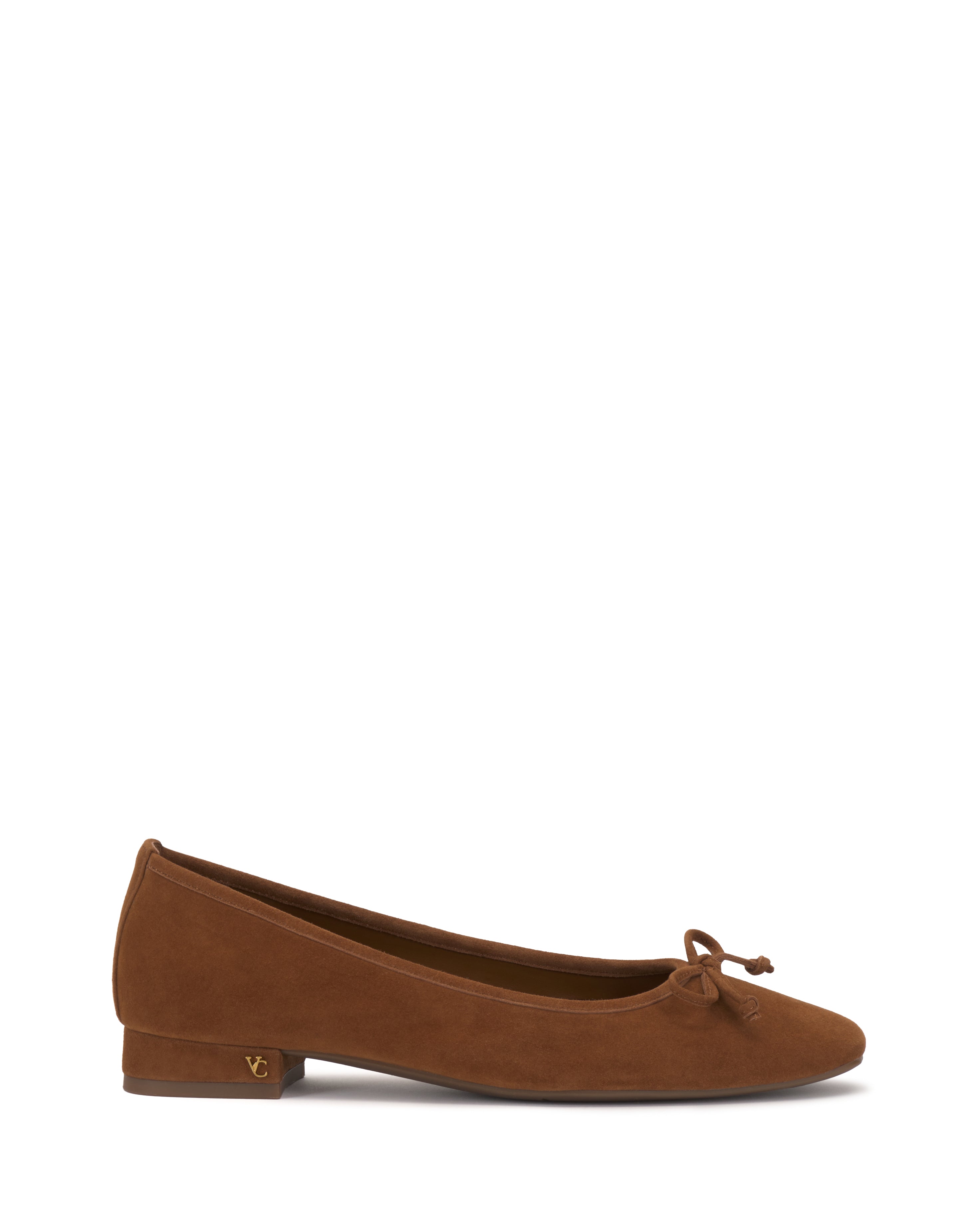 The Jenlea Ballet Flat by Vince Camuto features brown suede, a low heel, rounded toe with a small bow, and a gold logo accent on the side of the heel.