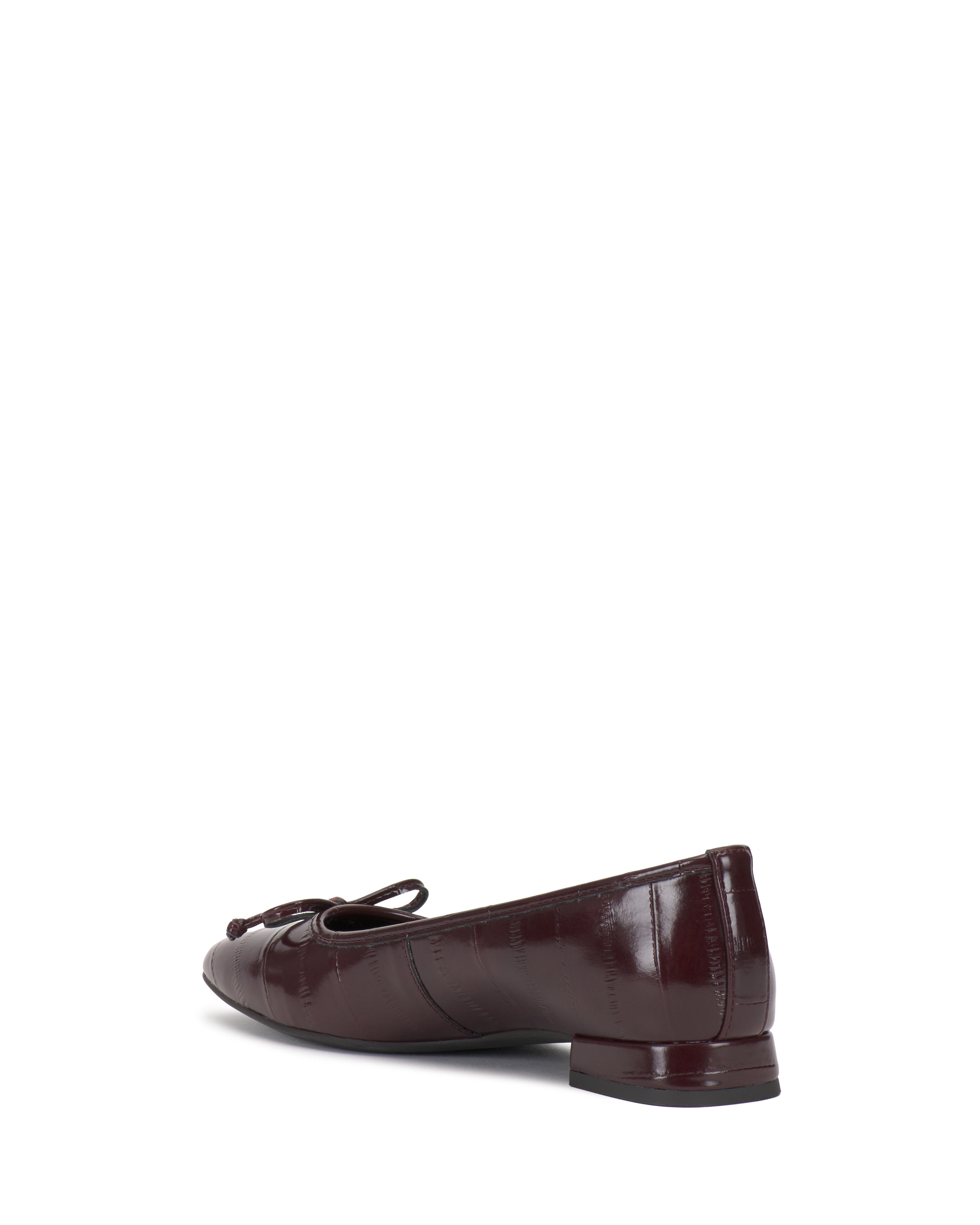 The Vince Camuto Jenlea Ballet Flat, shown in maroon patent leather with a low heel and bow detail on the toe, is pictured angled from the back and side against a white background.