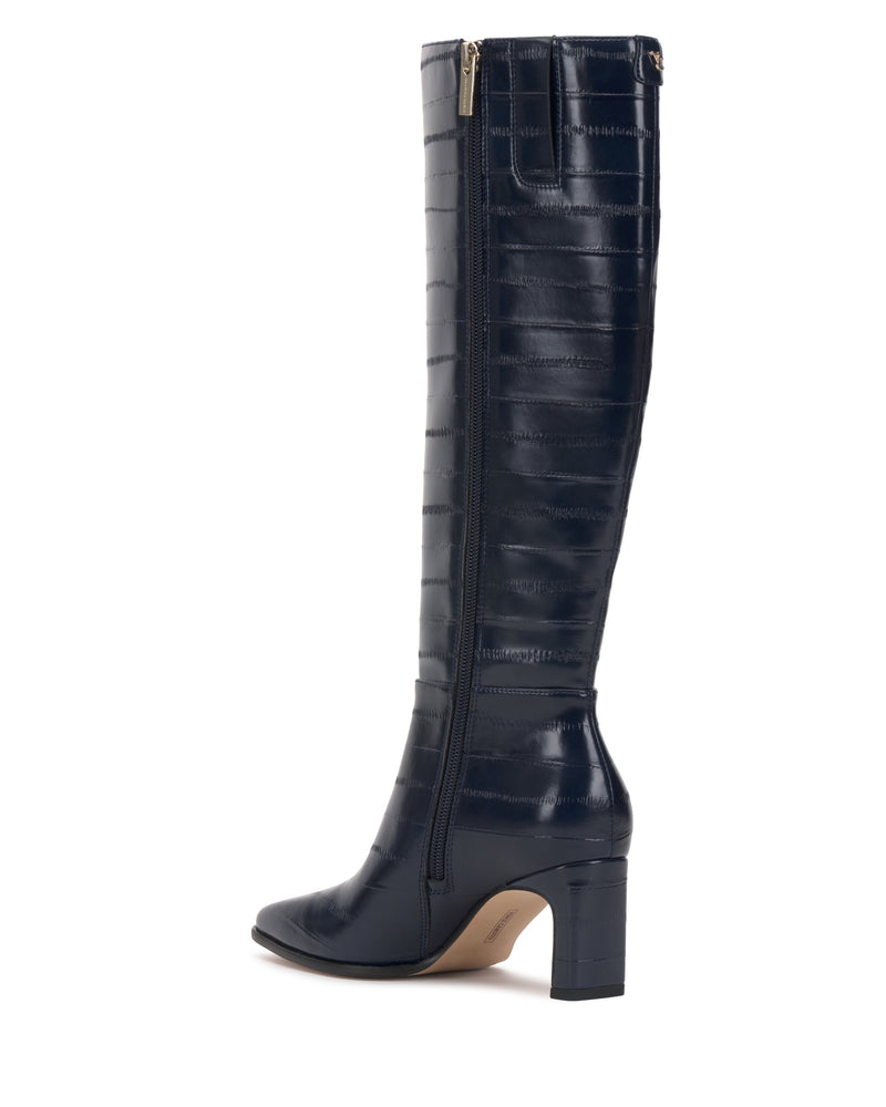 The Jorela Knee High Boot by Vince Camuto is a single, tall boot crafted from dark navy blue faux-crocodile leather, featuring a block heel, pointed toe, inner zipper, and subtle stitching details—shown angled to the left against a white background.