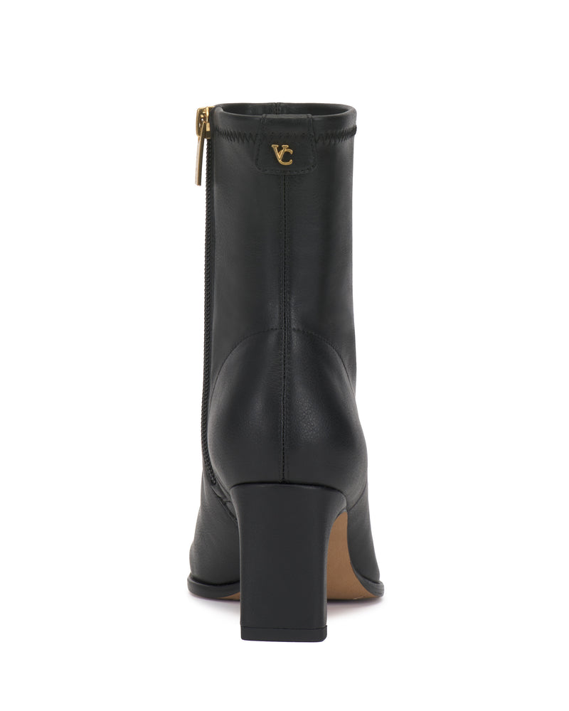 The Vince Camuto Julea Bootie is a black ankle boot viewed from the back, featuring a side zipper and a gold VC logo on the upper heel. It has a block heel and a smooth finish.