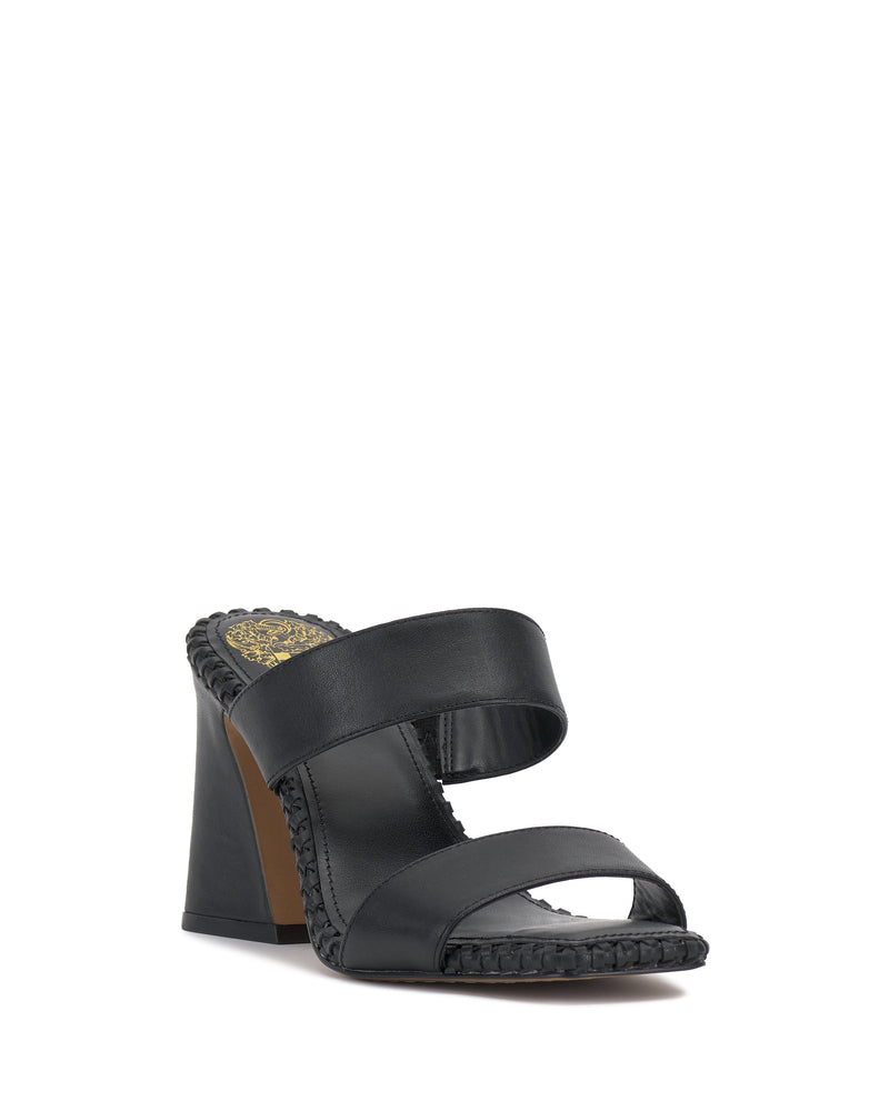 The Kaden Mule by Vince Camuto is a black block heel sandal with two wide leather straps, braided trim, open toe, and a woven midsole for a boho look. The insole features a decorative gold pattern near the heel.