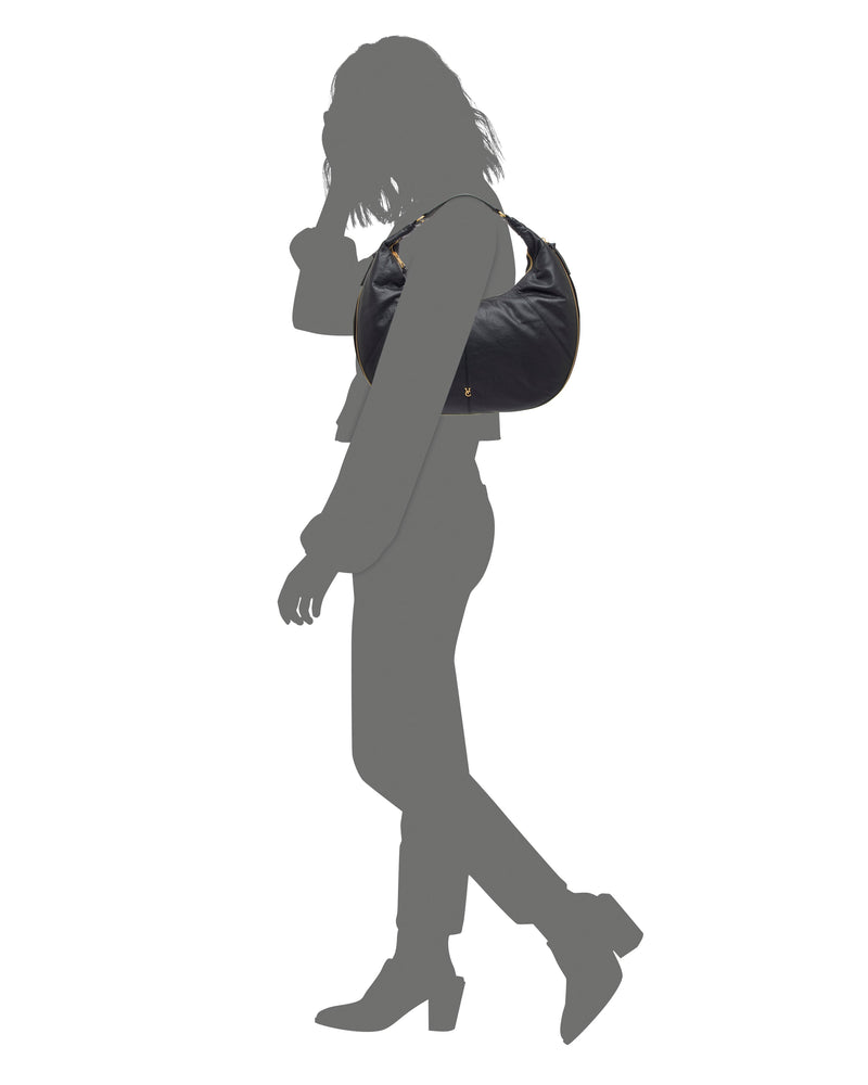 A gray silhouette walks in heeled boots, carrying the Vince Camuto Kaela Hobo Bag—a spacious black shoulder bag with gold hardware—over their shoulder against a white background.