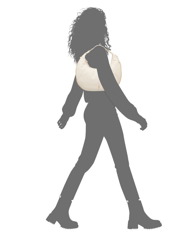 Silhouette of a person walking in boots, pants, and a long-sleeve top, carrying the Vince Camuto Kaela Hobo Bag in light beige over their shoulder.