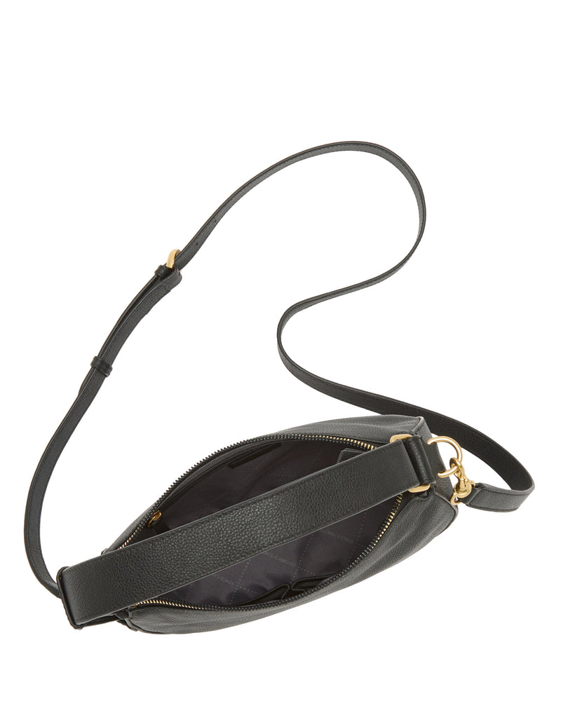 The Vince Camuto Karla Crossbody Bag features a black leather half-moon shape, gold zipper, adjustable strap, and an open top with a spacious, dark fabric-lined interior.