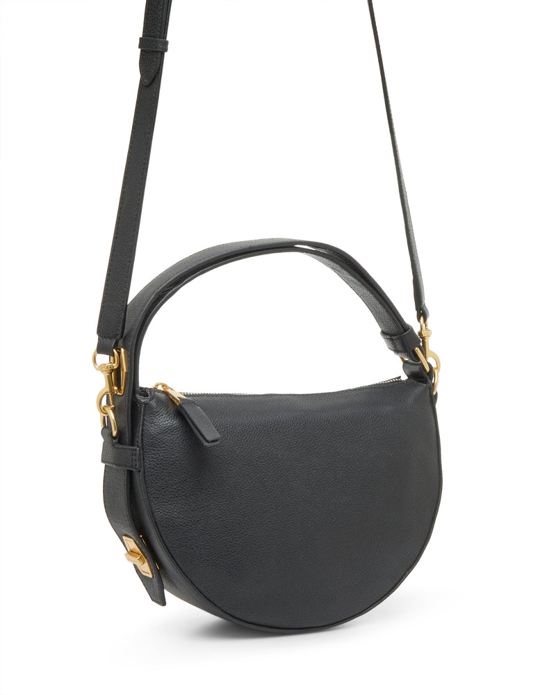 The Karla Crossbody Bag by Vince Camuto is a black, half-moon shape bag with a top handle, adjustable shoulder strap, gold-tone hardware, and a zippered main compartment.