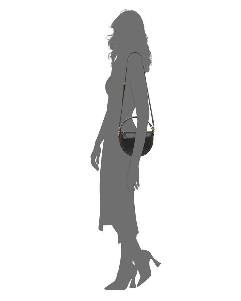 Silhouette of a woman in profile, wearing heels and a mid-length dress, carrying the Vince Camuto Karla Crossbody Bag—featuring a distinctive half-moon shape—on her shoulder against a plain white background.