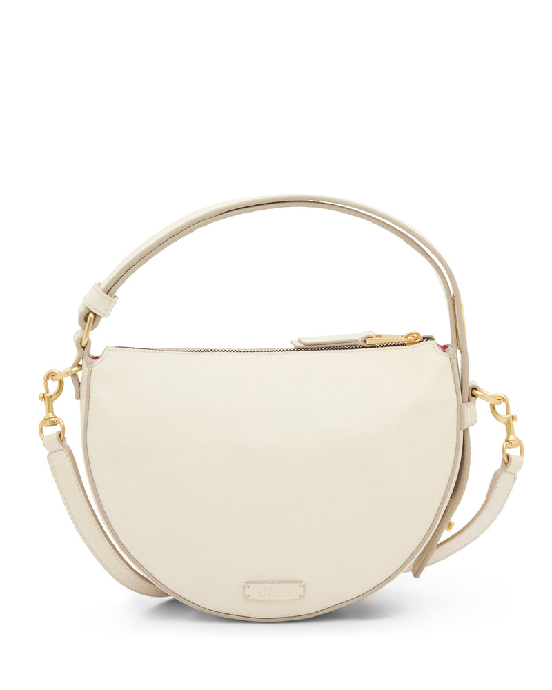 The Karla Crossbody Bag by Vince Camuto is a cream, crescent-shaped leather handbag featuring gold hardware, detachable and adjustable shoulder strap, zip-top closure, and a minimalist design.