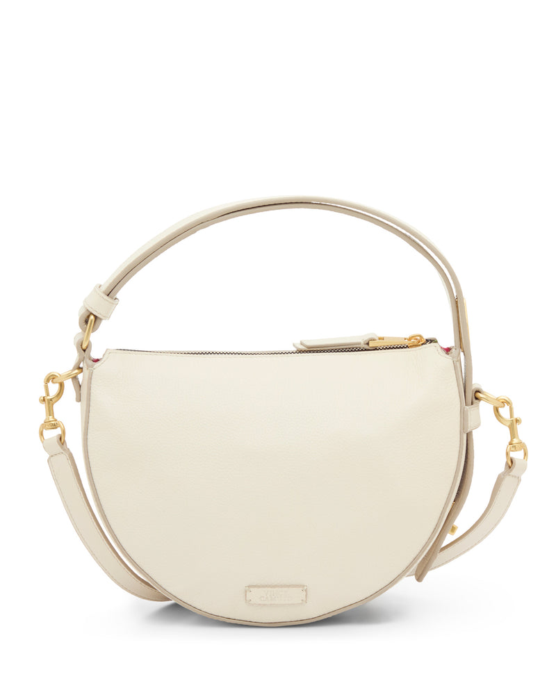 The Vince Camuto Karla Crossbody Bag features a chic half-moon shape in cream leather with a zip closure, short handle, detachable shoulder strap, and gold hardware, shown on a white background.