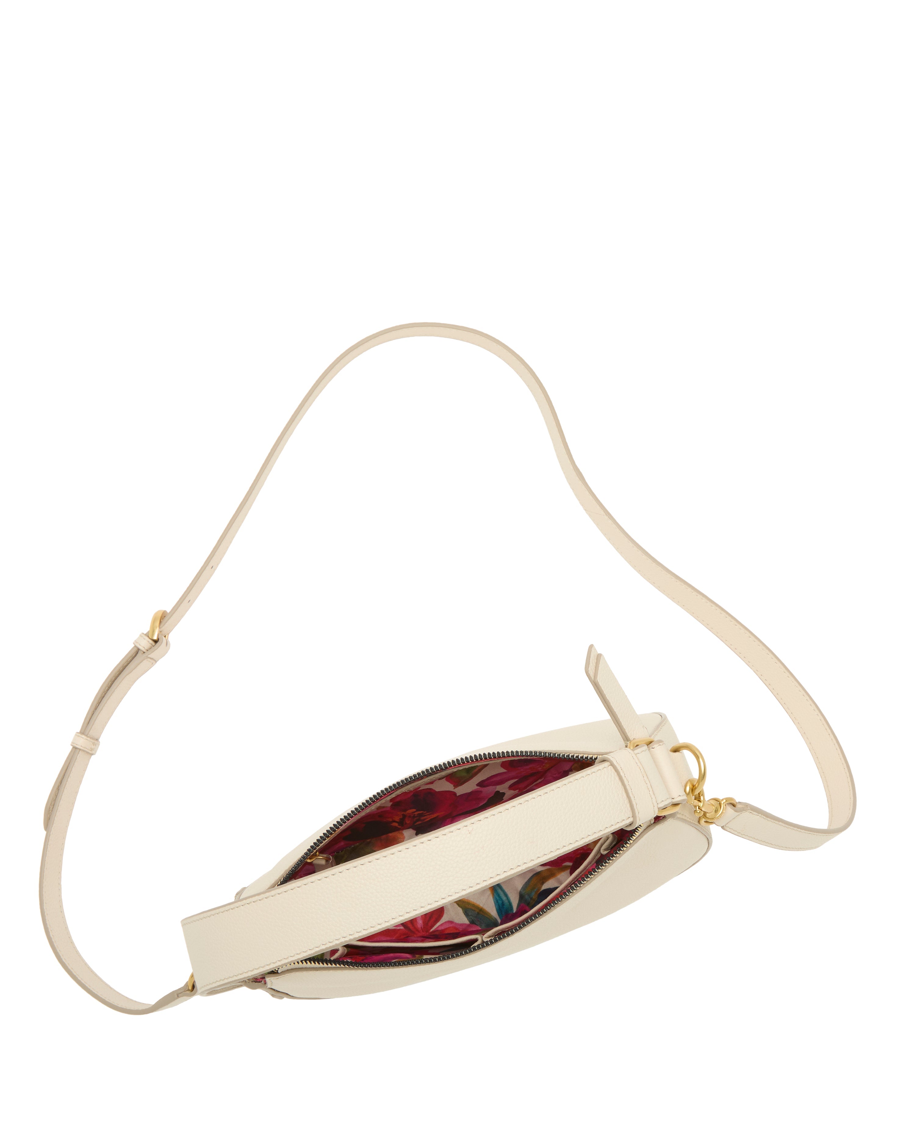 The Karla Crossbody Bag by Vince Camuto showcases a cream half-moon shape with a long adjustable strap and zippered top. Viewed from above, it reveals a bold red and teal patterned fabric lining inside.