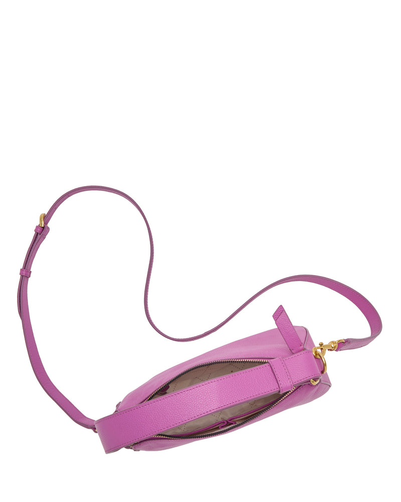 The Karla Crossbody Bag by Vince Camuto features a pink half-moon shape, gold zipper, and adjustable strap. Shown from above, the zipper is partially open to reveal its light-colored interior.